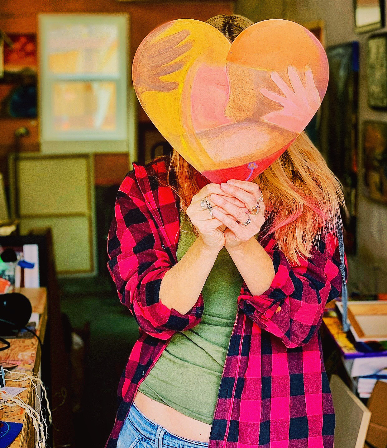 woman holding piece of artwork shaped like a heart that covers her face